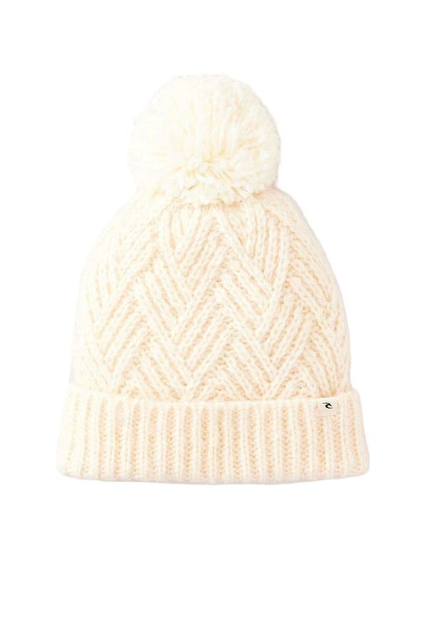 A beige colored Rip Curl beanie with a large pom pom at the top and a woven clamp around the ribbed section.