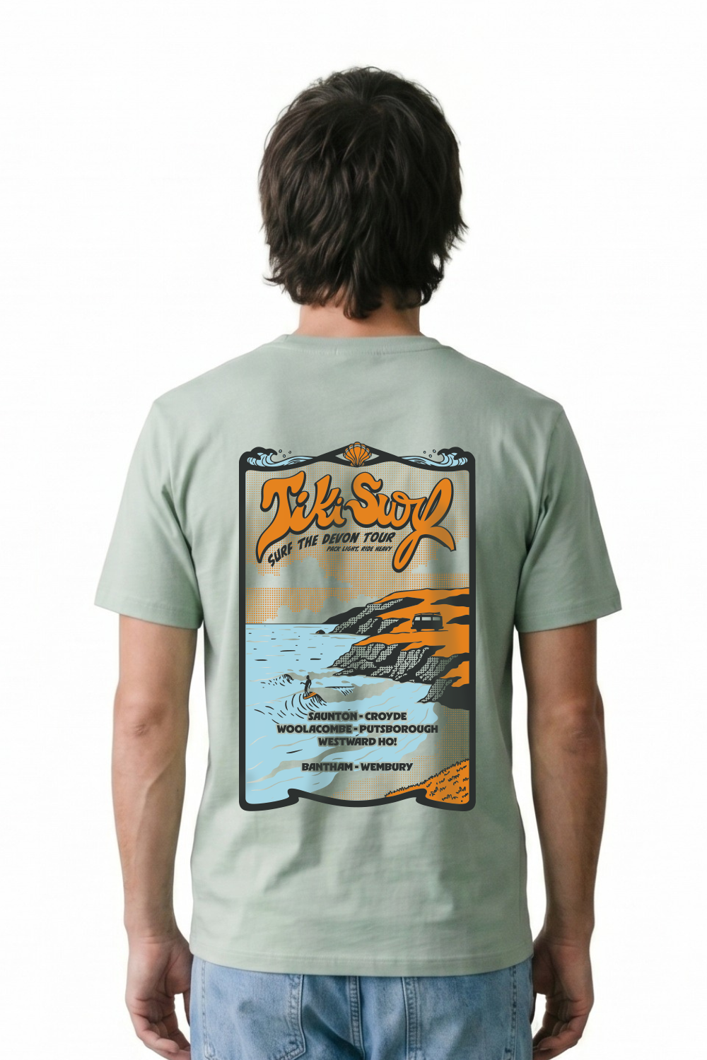 Man wearing a Tiki T-Shirt in a light green colour. Featuring a bold retro back print showcasing Devon’s famous surf beaches.