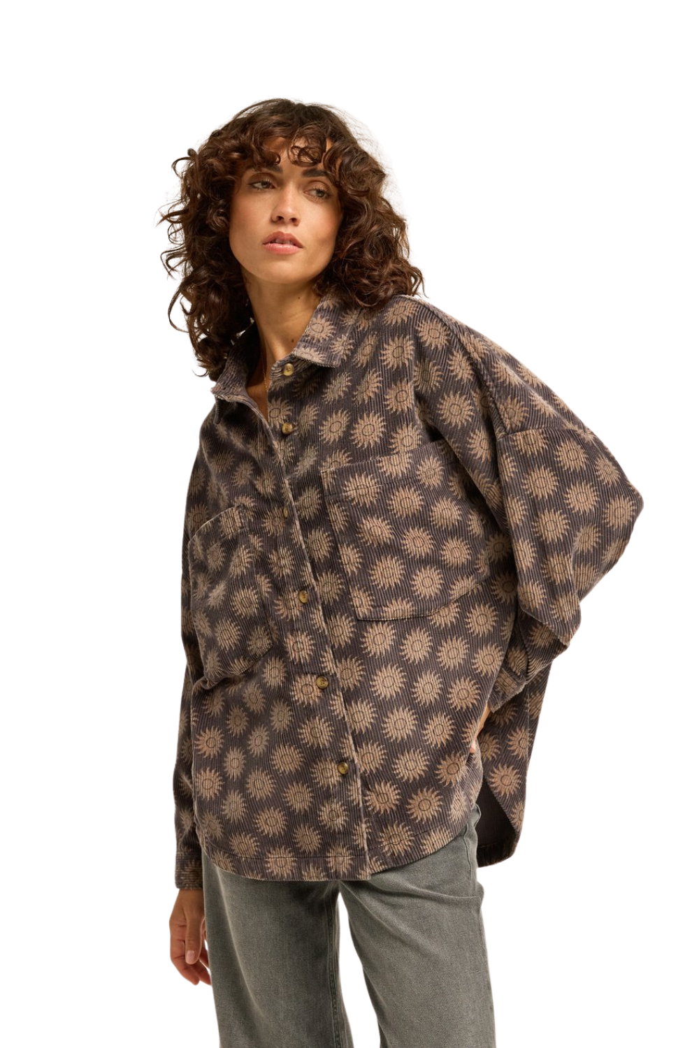 A woman wearing a loose-fitting, long-sleeve button-up Billabong shirt with a charcoal and beige sunburst pattern, paired with gray pants, photographed against a solid white background.