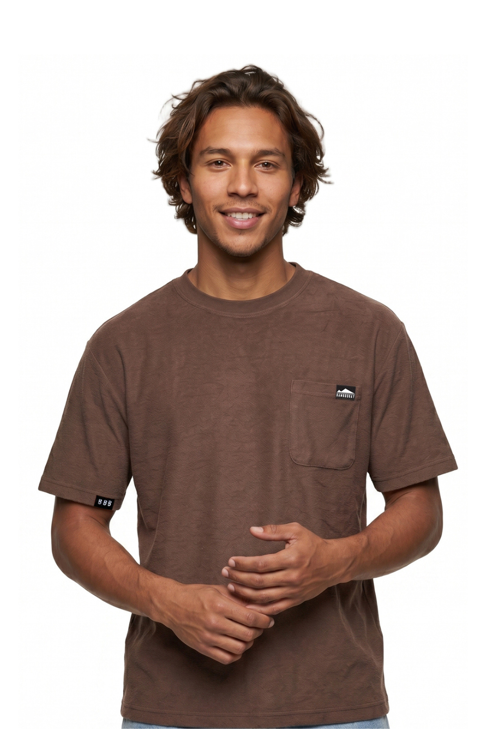 Man wearing a brown t-shirt with a chest pocket a small logo bagde on a white background