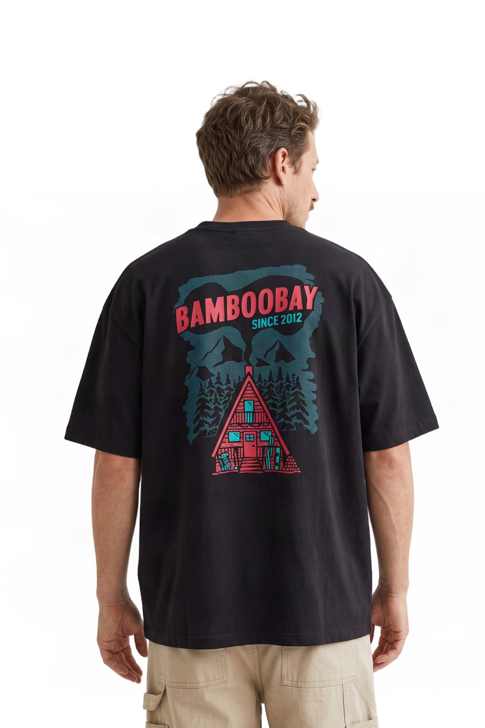 A man viewed from behind wearing a black short-sleeve t-shirt with a large graphic print on the back. The graphic features the text 'BAMBOOBAY SINCE 2012' in red and teal, above a red cabin and pine tree illustration.