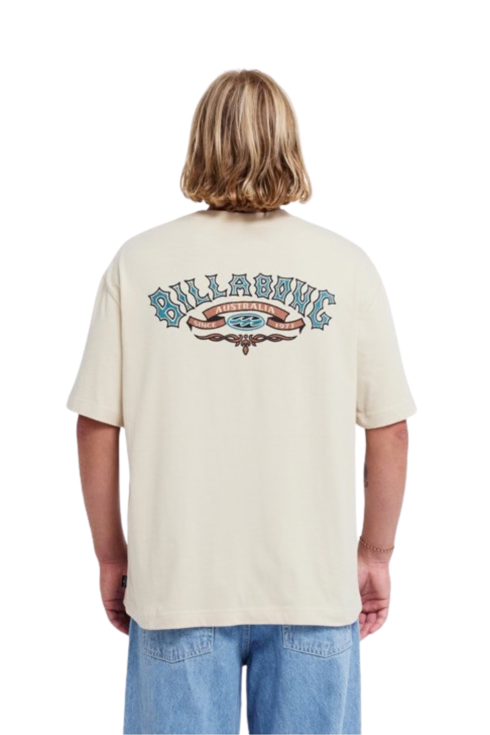 A person shown from the back wearing a cream-colored Billabong t-shirt with a large graphic logo on the upper back, paired with blue jeans against a plain white background.