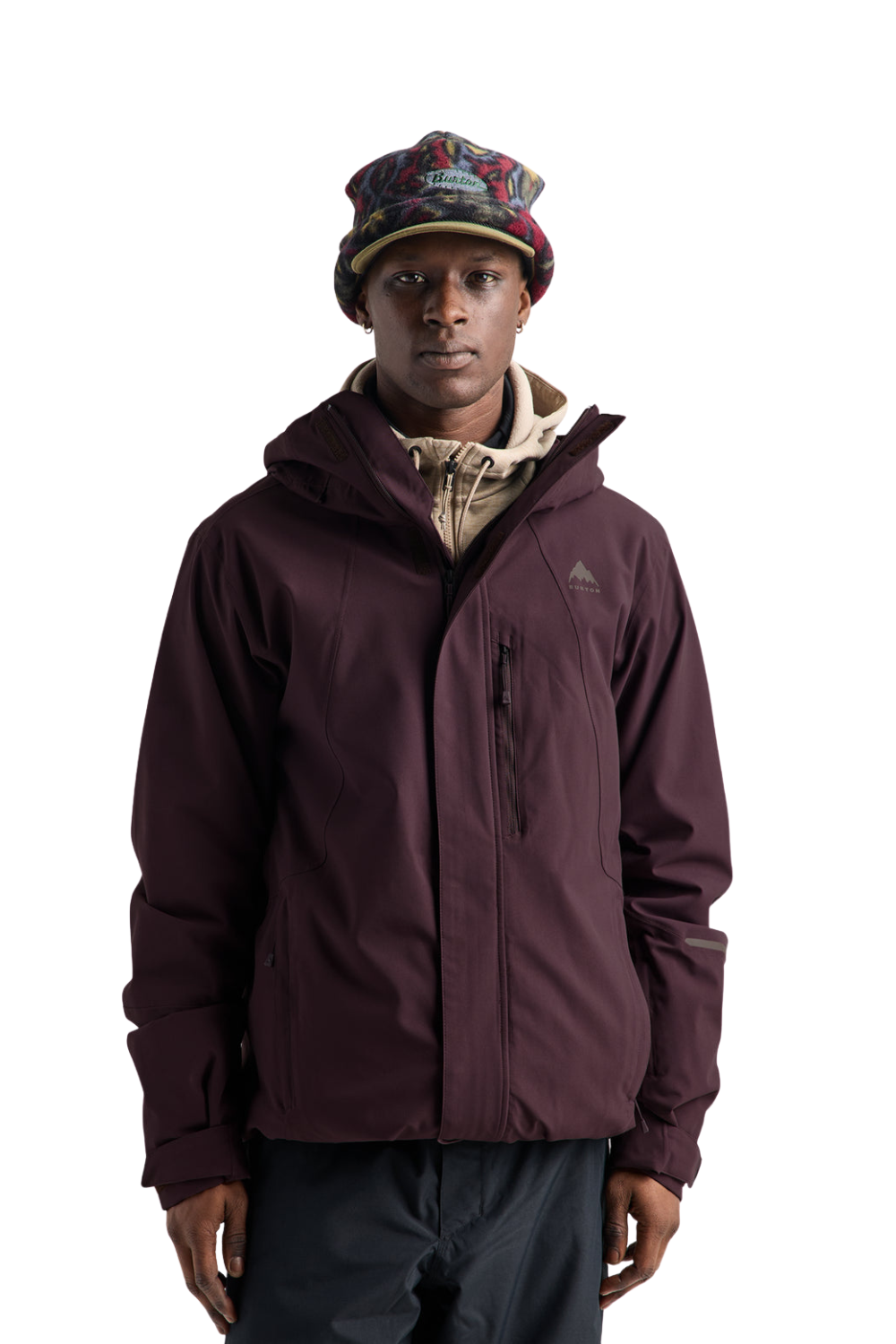 A man wearing a dark plum hooded jacket, a patterned knit beanie, and dark pants, standing against a solid white background.