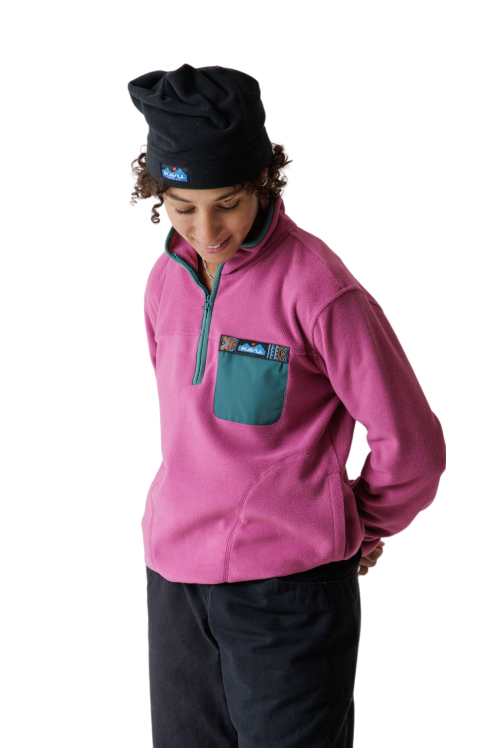 A person wearing a pink quarter-zip fleece pullover with a teal chest pocket, a black beanie, and dark pants, photographed against a plain white studio background.