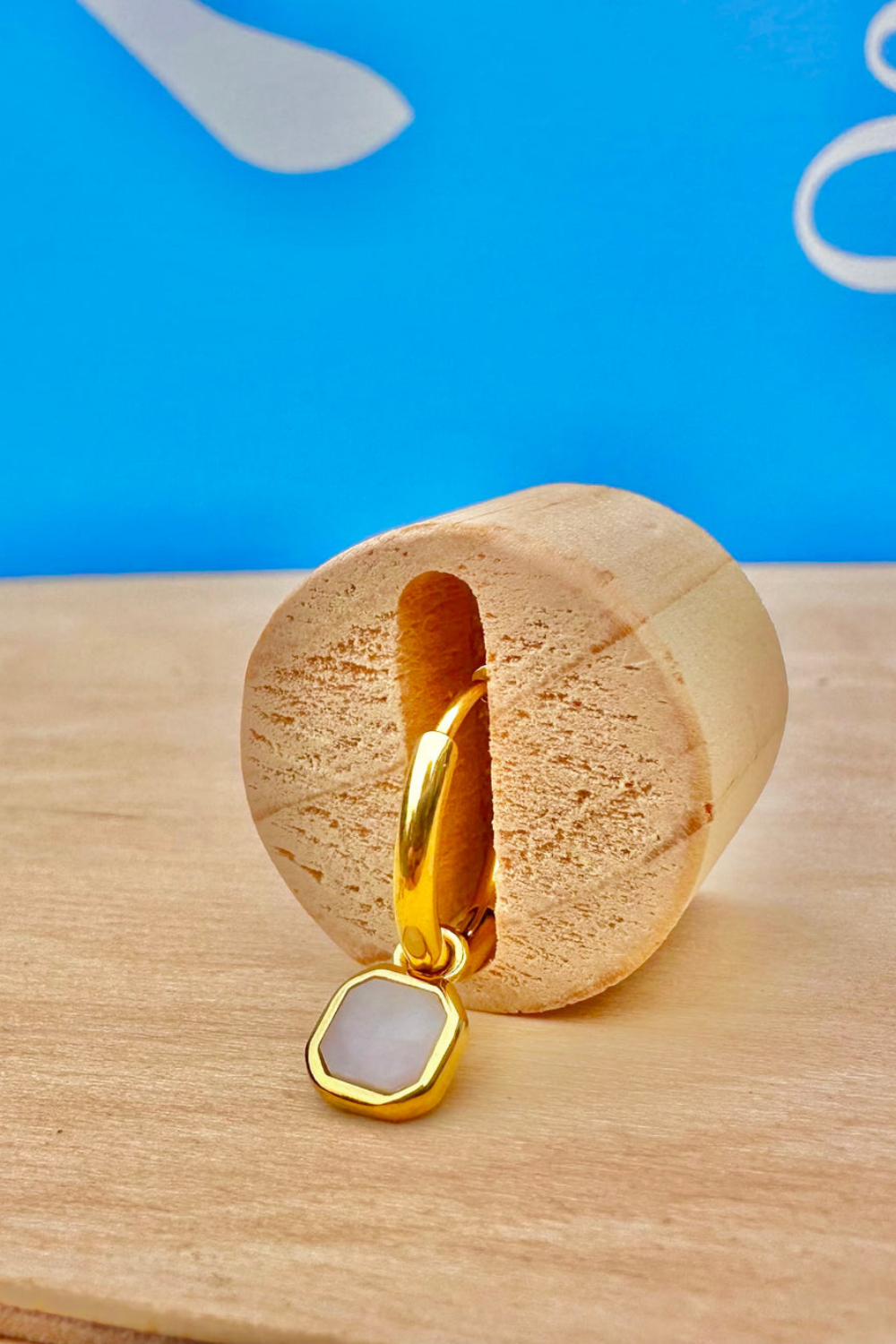 Gold earring with a opal stone on a wooden stand against a blue background