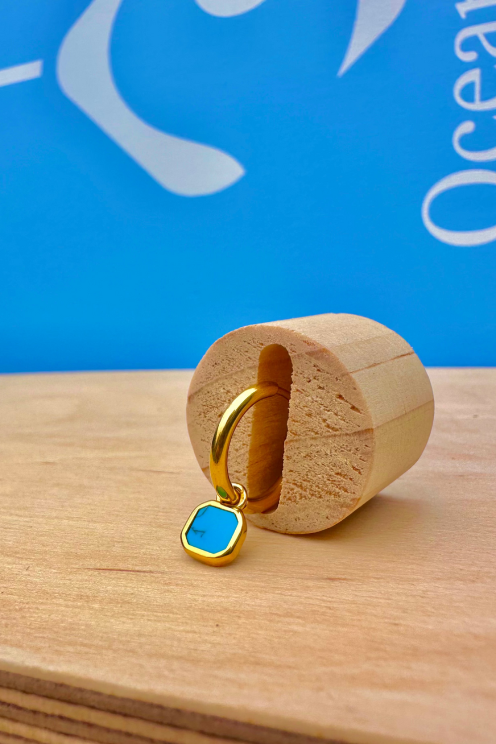 Gold ring with a blue gemstone on a wooden block against a blue background