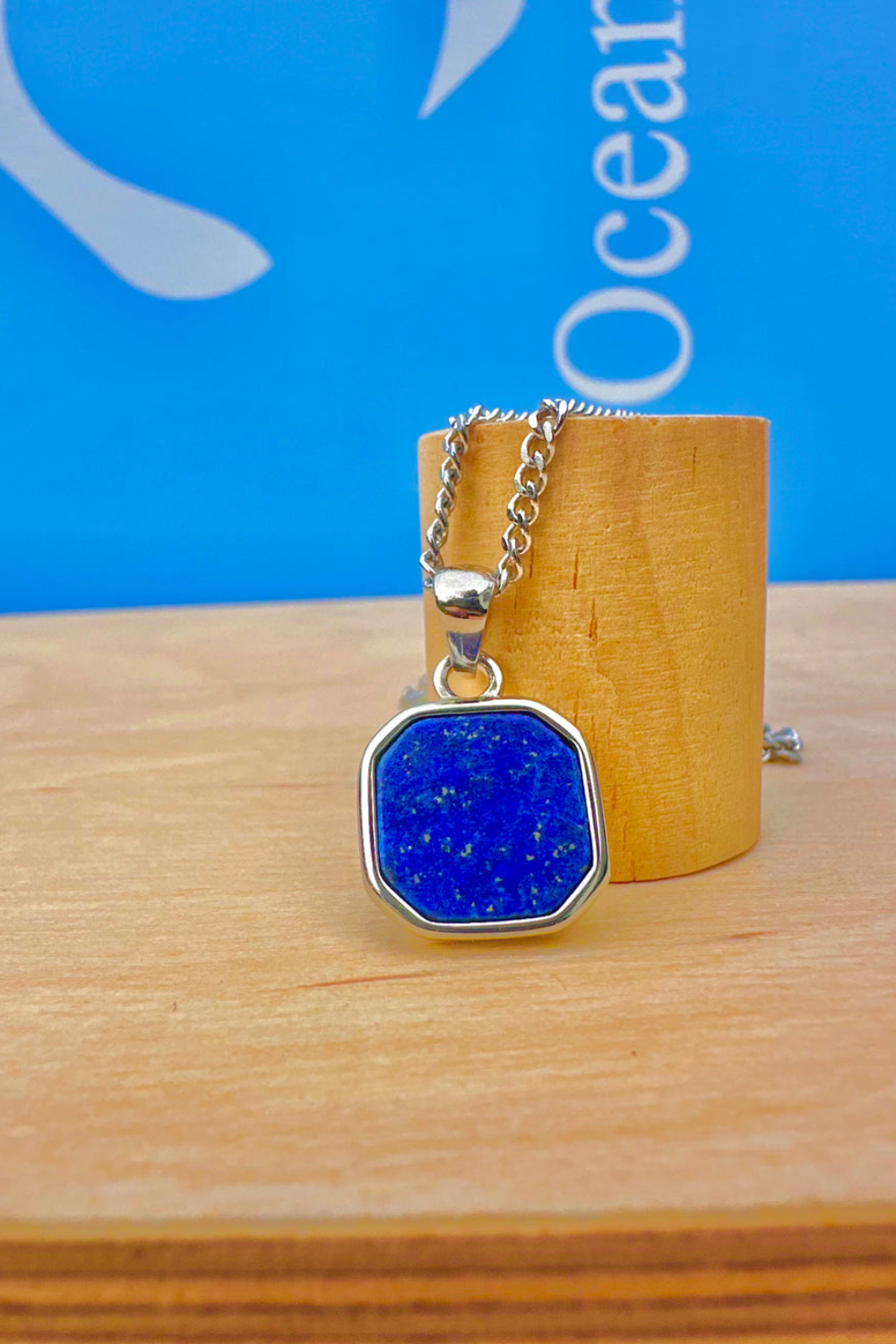 Blue Lapis Lazuli Stone pendant necklace on a wooden stand with a blue background