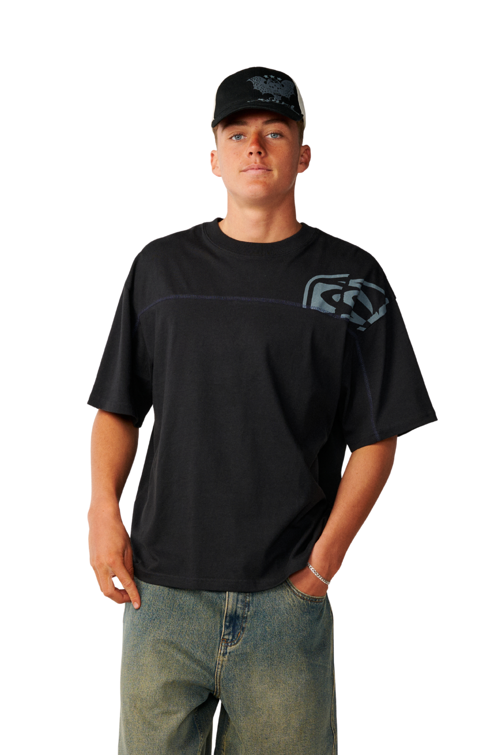 A man wearing a black short-sleeve t-shirt with a gray graphic logo on the left chest, paired with blue jeans and a black baseball cap, photographed against a solid white background.