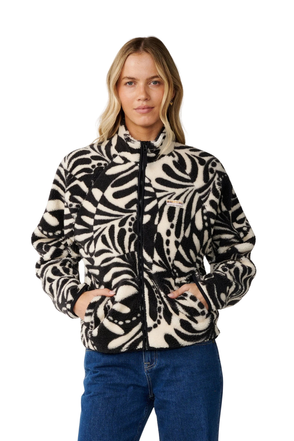 A woman wearing a black and cream abstract patterned fleece jacket with a black zipper, paired with blue jeans, photographed against a solid white background.