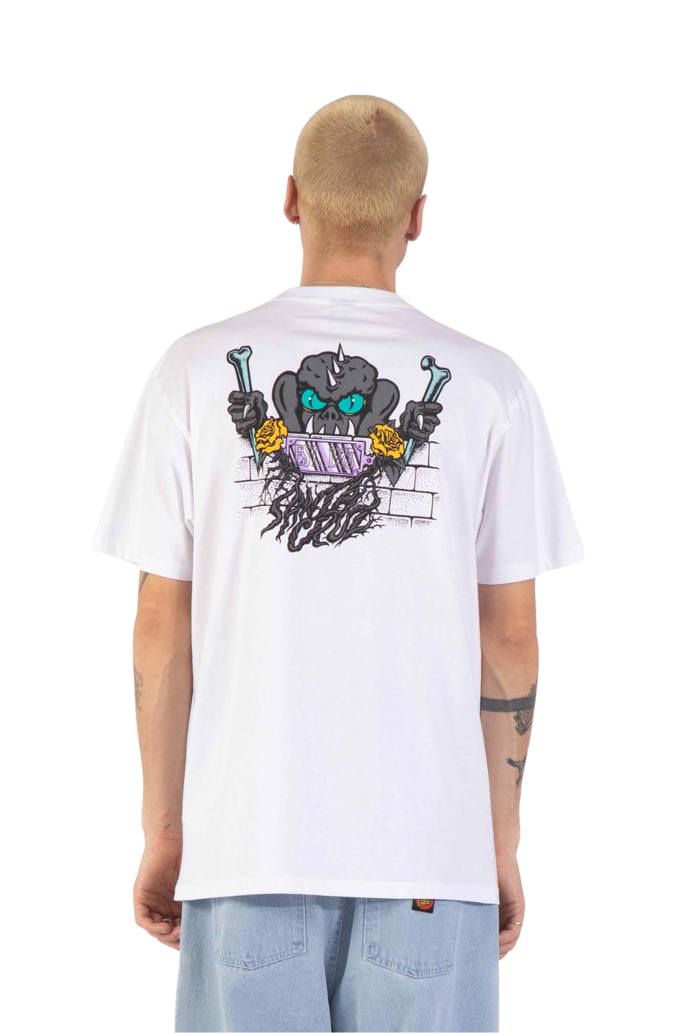 A man viewed from behind wearing a white t-shirt with a large graphic print on the back, featuring a cartoon skull with green eyes and a purple striped mouth, holding wrenches. He is also wearing light blue jeans against a plain white background.