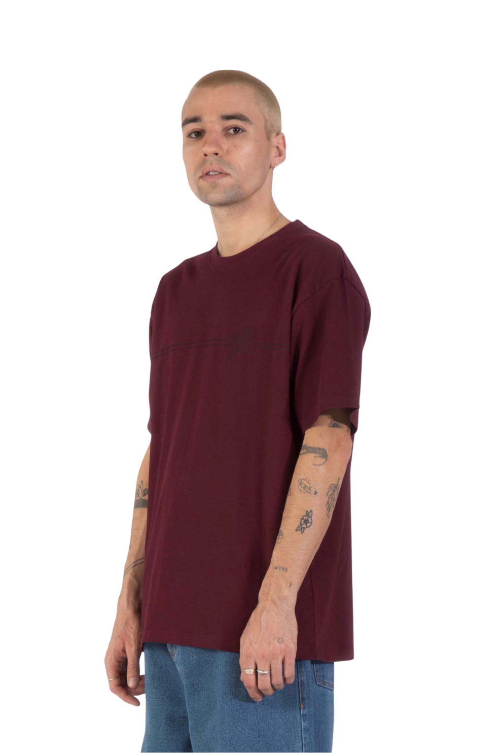 A man wearing an oversized maroon short-sleeve t-shirt and blue jeans, standing against a plain white background.