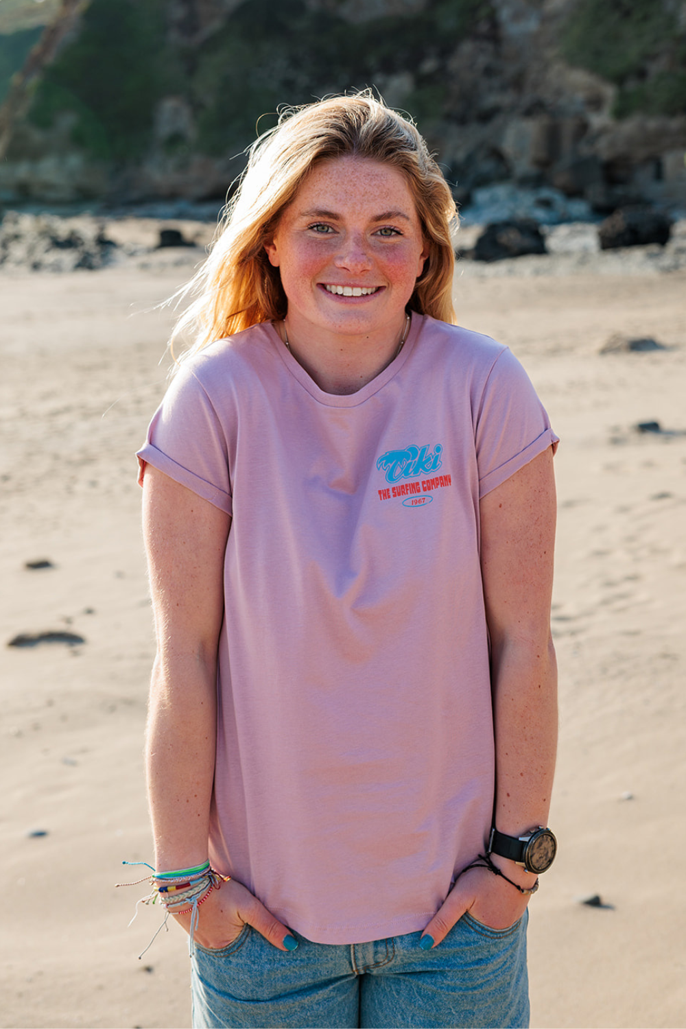 Person wearing a pink t-shirt with a Tiki logo on a beach