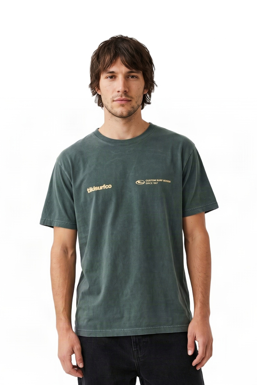 A man wearing a dark green crewneck t-shirt with gold printed Tiki logos on the chest, standing against a plain white background.