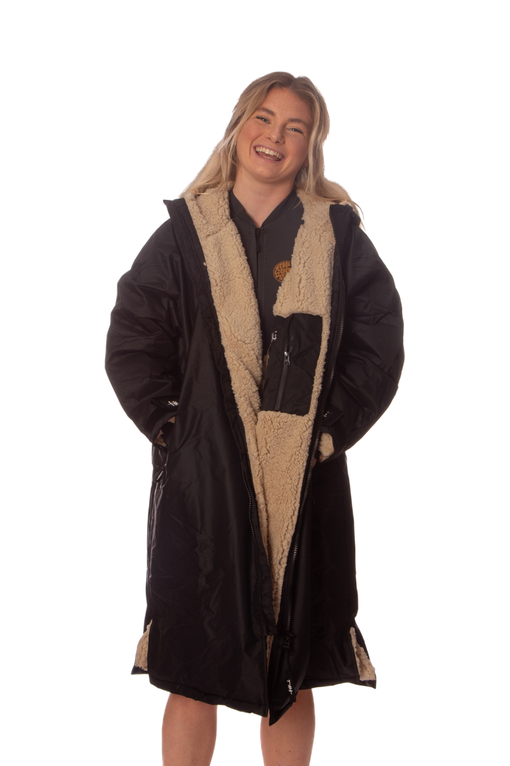 A woman modeling a long black hooded changing robe/ coat with a thick beige sherpa lining, shown against a plain white background.