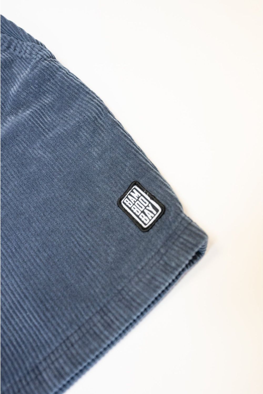 Bamboobay Cord Shorts in Navy. Image shows the fron left leg logo close up. The image is a flatshot taken in a studio