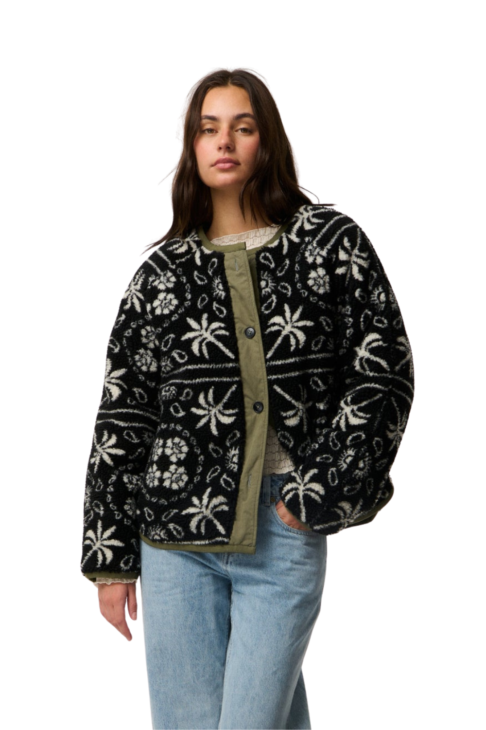 A woman modeling a black fleece jacket with a white tropical palm tree and floral pattern, featuring an olive green button-up front, paired with light blue jeans against a plain white background.
