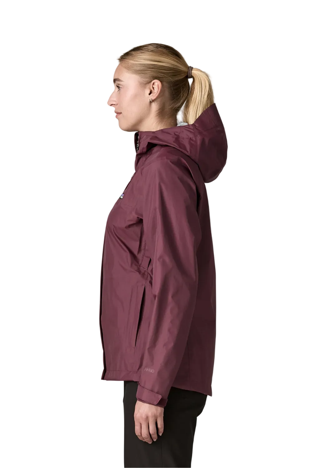 A woman in profile wearing a hooded rain jacket in a deep plum or burgundy shade, paired with black pants, against a solid off-white background.