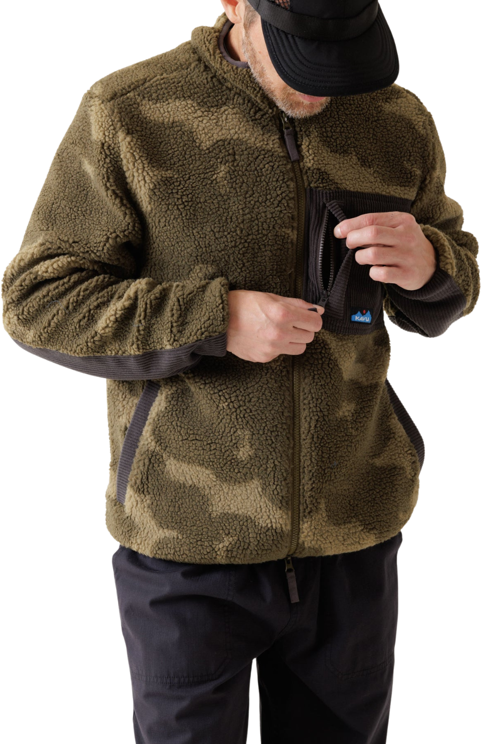 A man wearing a brown and olive green camouflage Kavu sherpa fleece zip-up jacket with black trim on the sleeves and pocket, paired with black pants and a black cap.