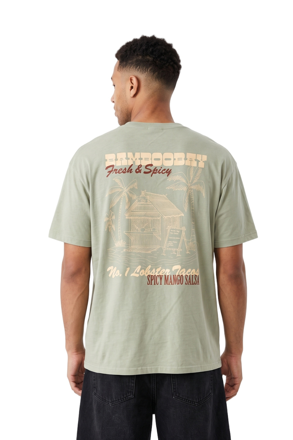 A man viewed from the back wearing a sage green t-shirt with a large beige graphic print on the back, paired with dark jeans, against a plain white background.