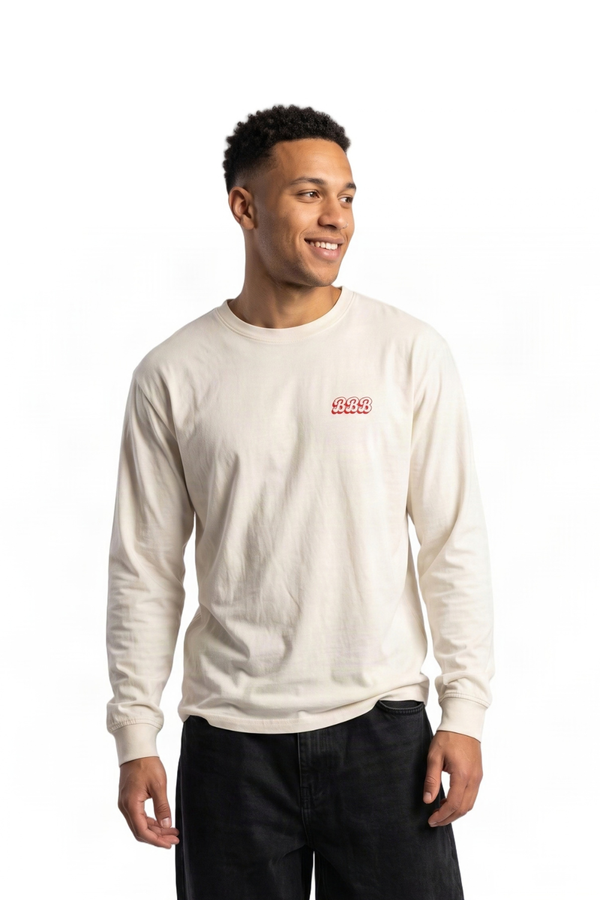 A man wearing a cream-colored long-sleeve crewneck sweatshirt with a small red embroidered logo on the left chest, paired with black jeans, against a plain white background.