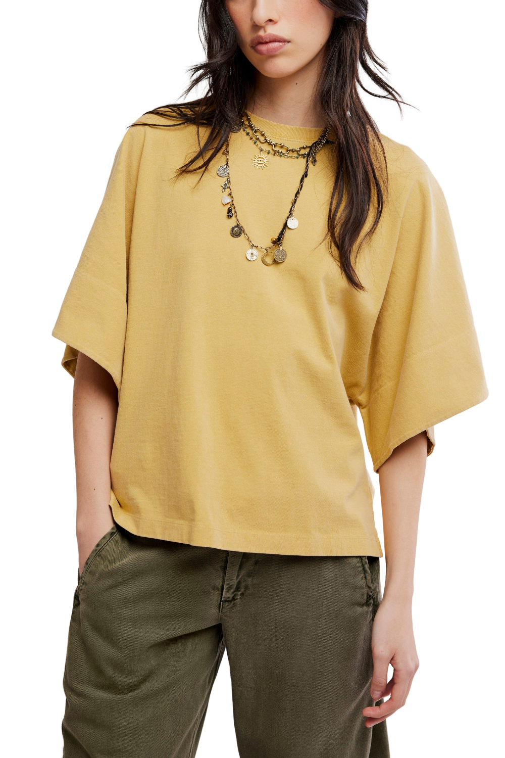 A woman wearing a mustard yellow oversized short-sleeve t-shirt and olive green pants, accessorized with layered necklaces, against a plain white background.