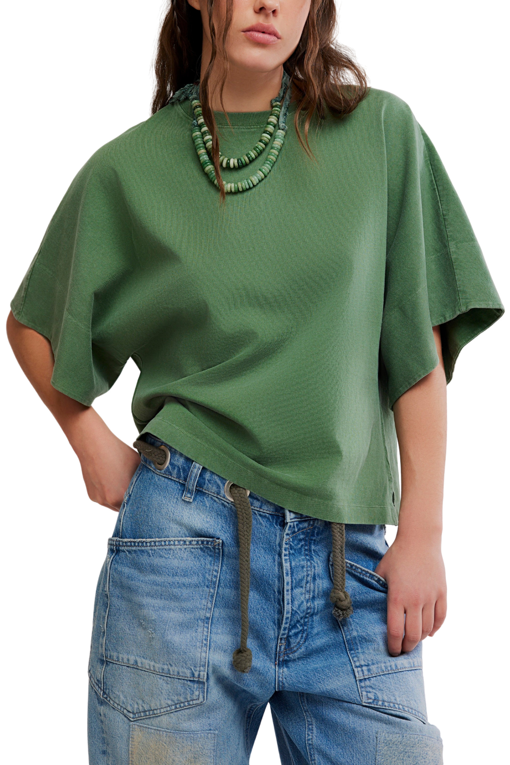 A woman wearing a green short-sleeve top with a relaxed, oversized fit and blue jeans, shown from the neck down against a plain white background.