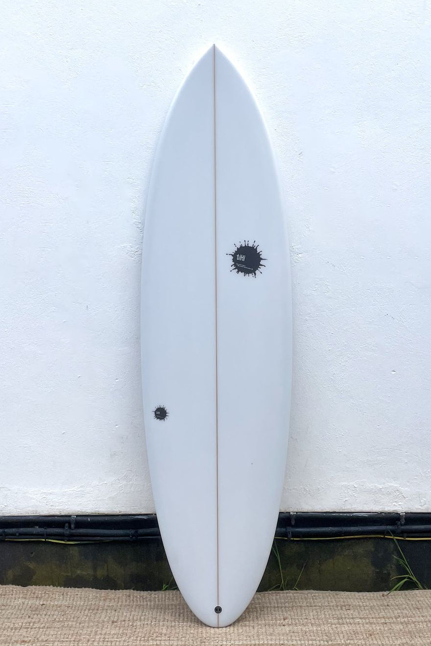 A white surfboard with a black logo, displayed vertically against a white wall.