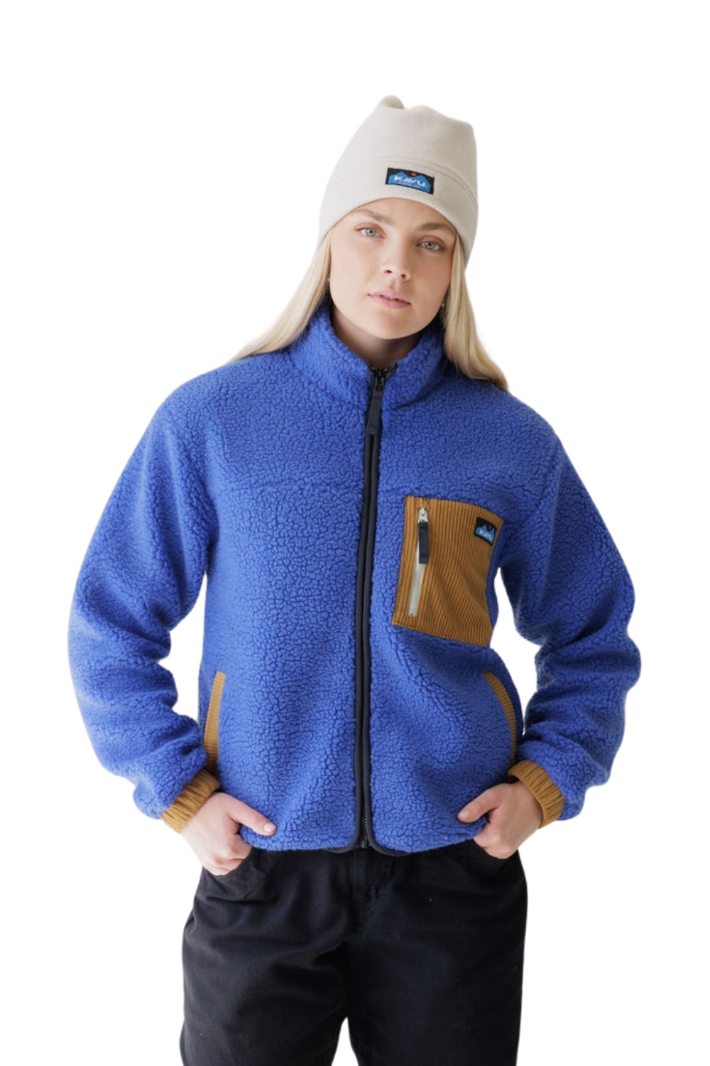 A woman wearing a blue fleece jacket with brown accents, a beige beanie with a Kavu logo, and black pants, photographed against a solid white background.