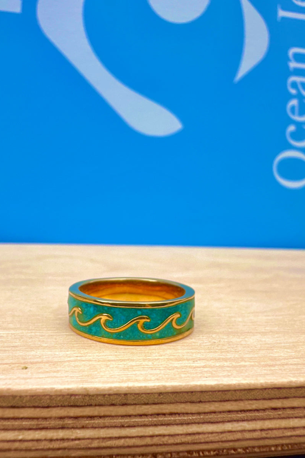 Ring in gold with wave design on a wooden surface against a blue background