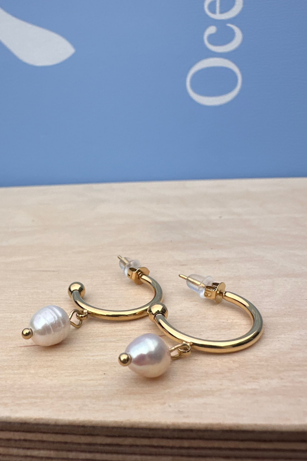 Gold hoop earrings with pearls on a wooden surface and blue background
