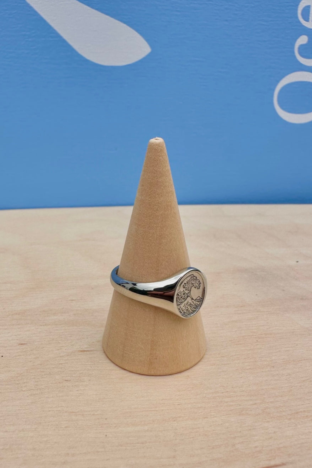 Silver ring with a circular wave design on a wooden cone against a blue background