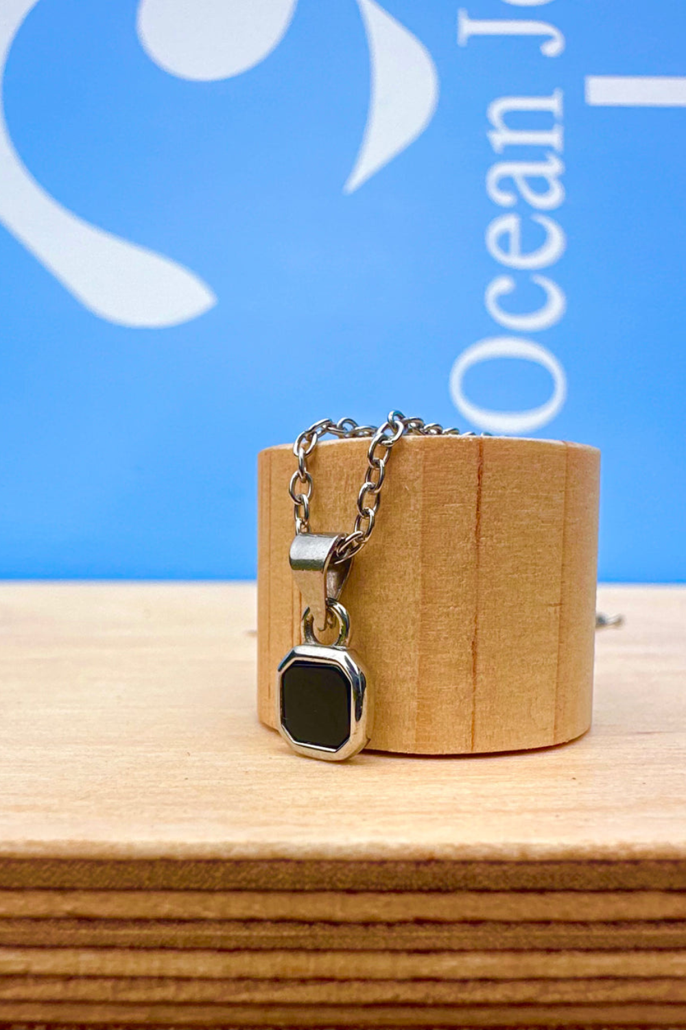 Silver Necklace with a small  Onyx stone pendant on a wooden stand 