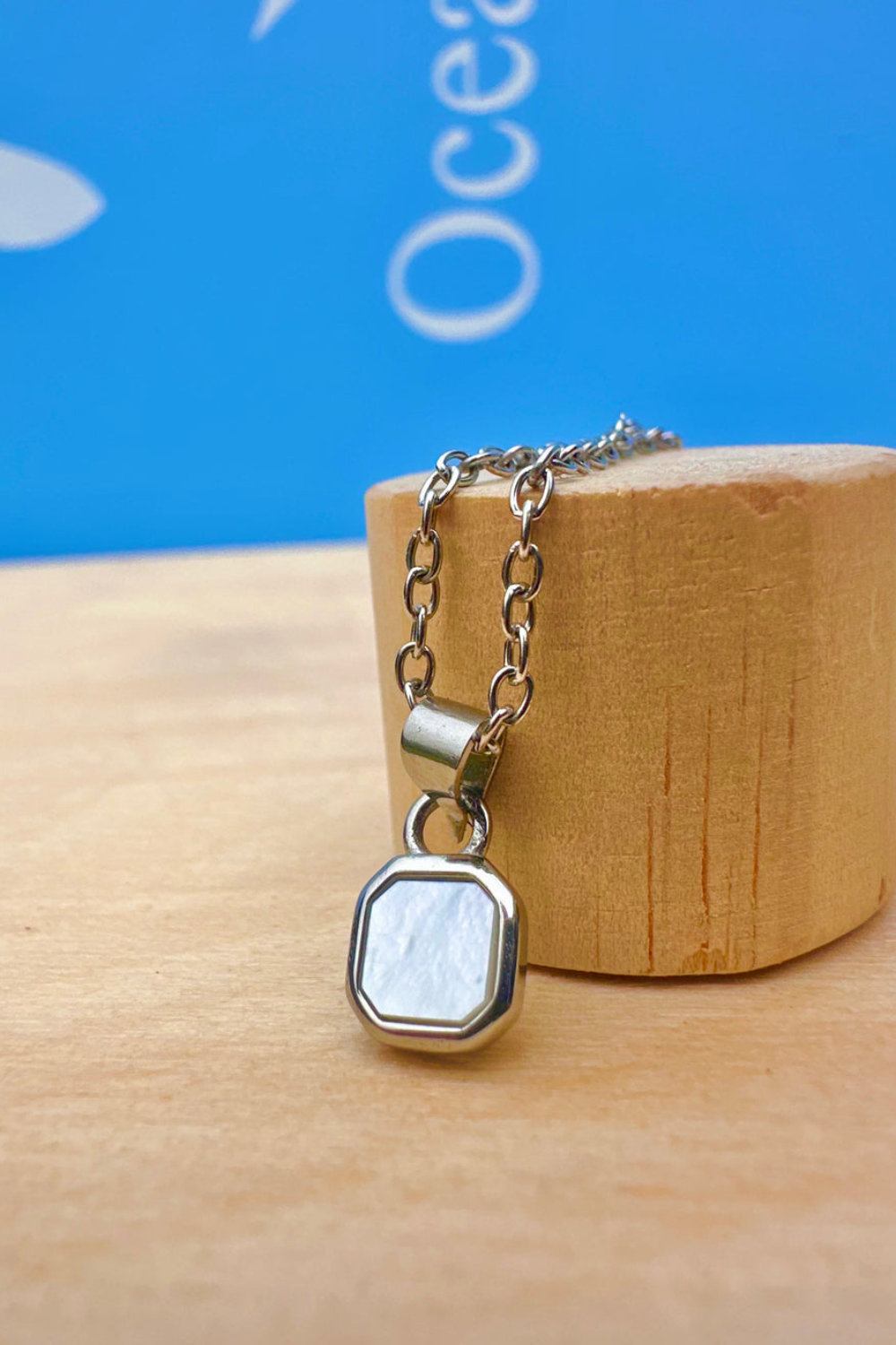 Necklace with a hexagonal pearl shell pendant on a wooden block against a blue background
