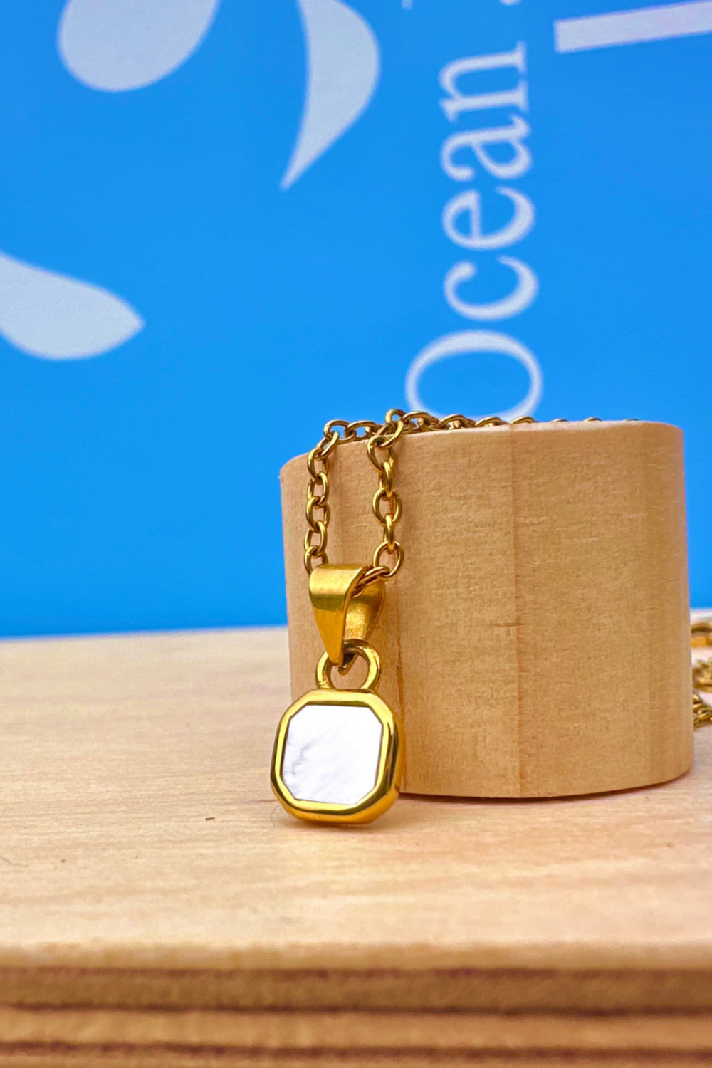 Gold necklace with a pearl shell stone pendant on a wooden stand against a blue background 