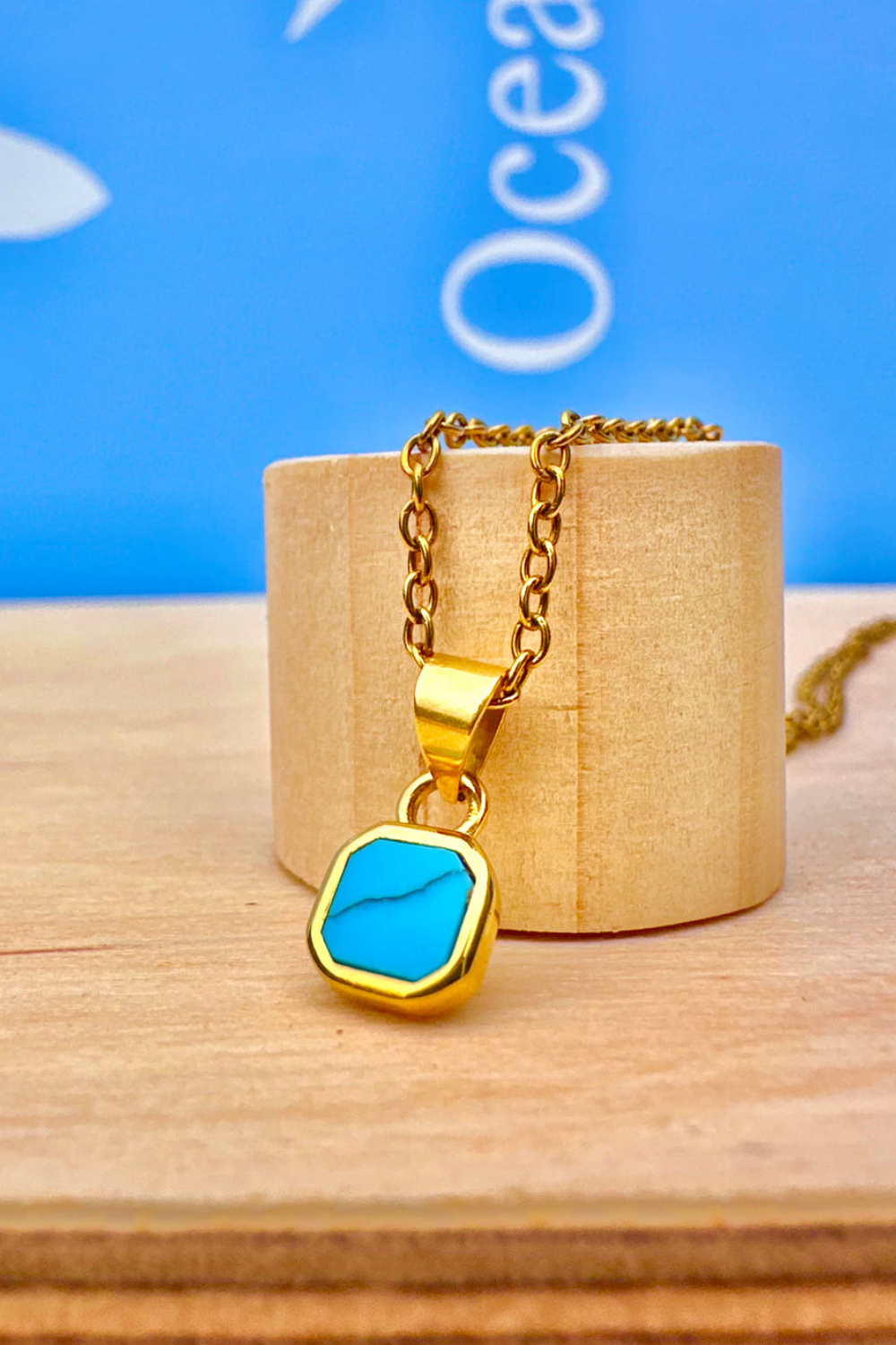 Gold necklace with a blue pendant on a wooden stand against a blue background 