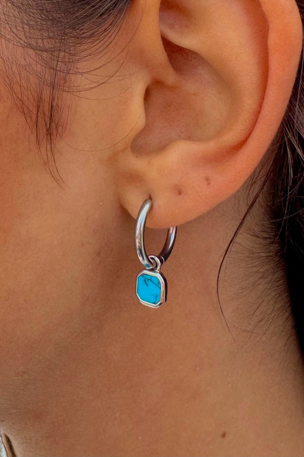 Close-up of an ear wearing a silver hoop earring with a turquoise stone.