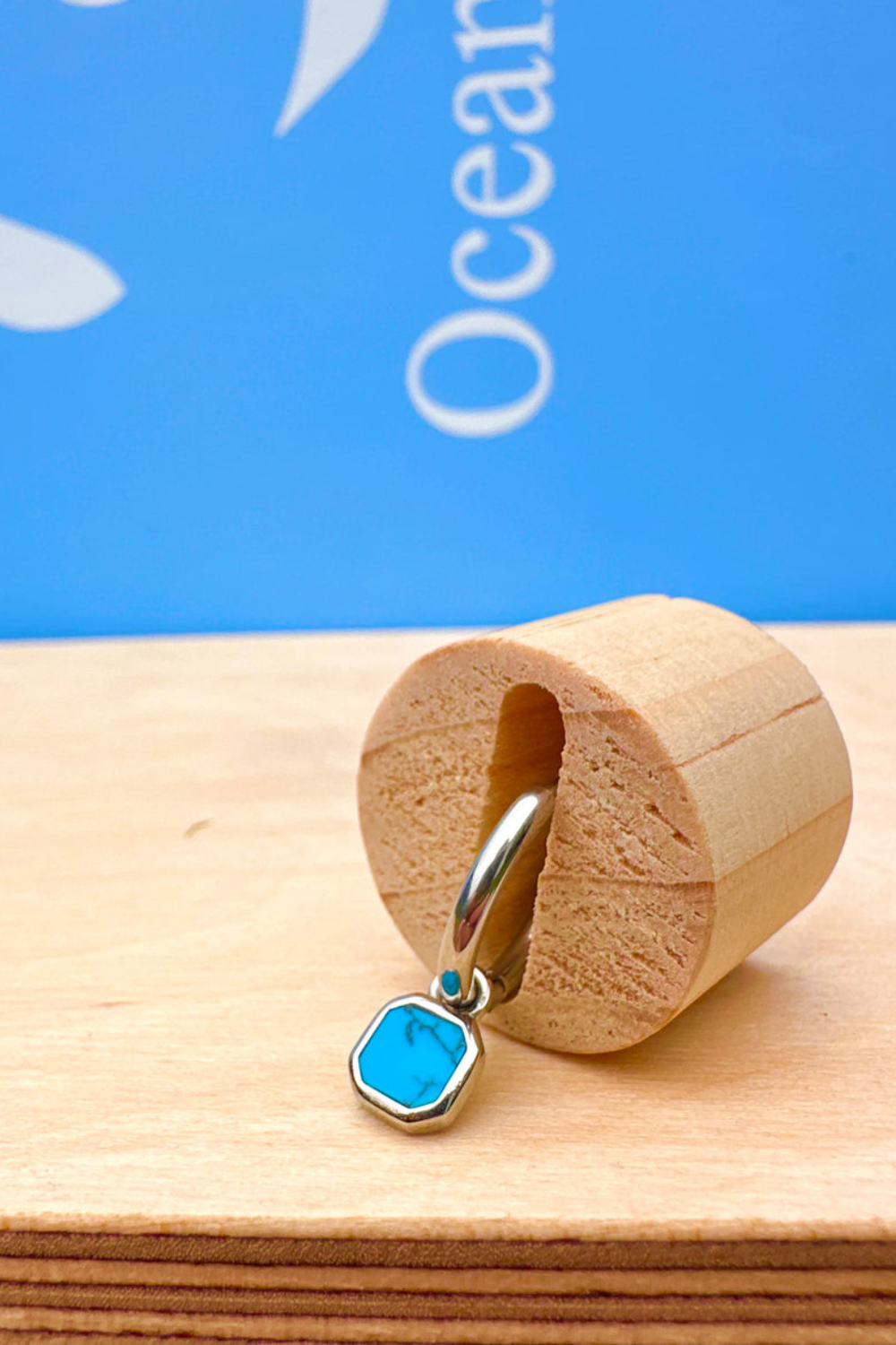 Blue stone earring in a wooden display holder against a blue background 