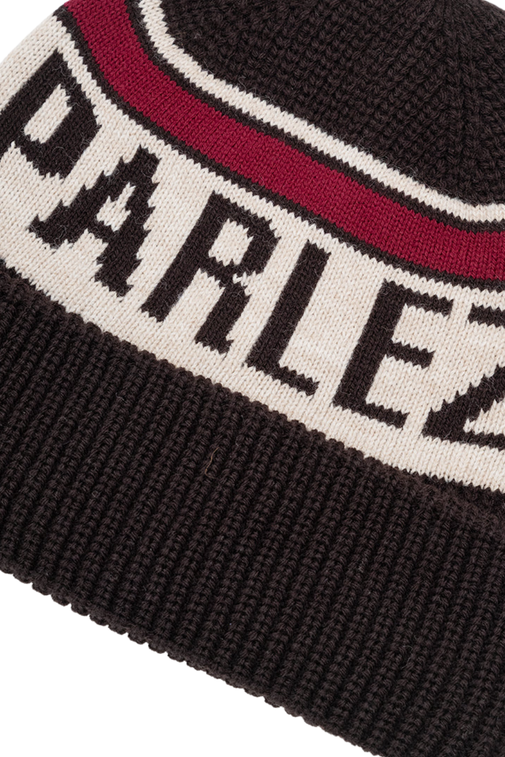 Close-up of a ribbed knit beanie with the word 'PARLEZ' knitted in black across a cream band, separated by a burgundy stripe, on a dark brown background.