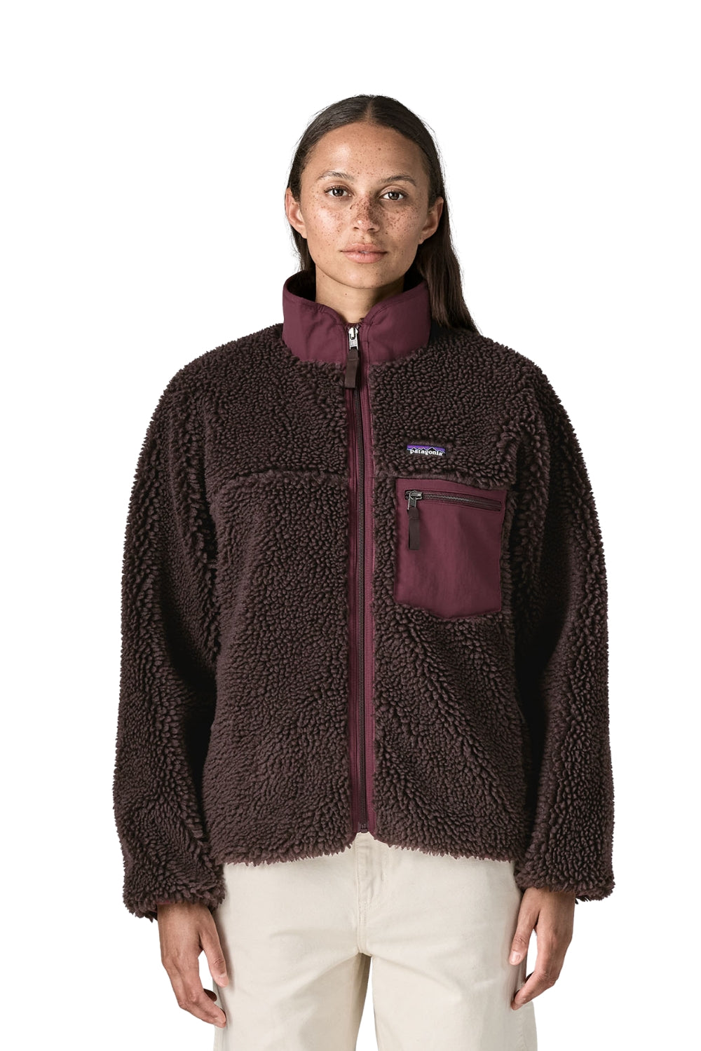 A woman modeling a dark brown sherpa fleece zip-up jacket with a contrasting burgundy collar, zipper, and chest pocket, paired with light beige pants against a plain white background.