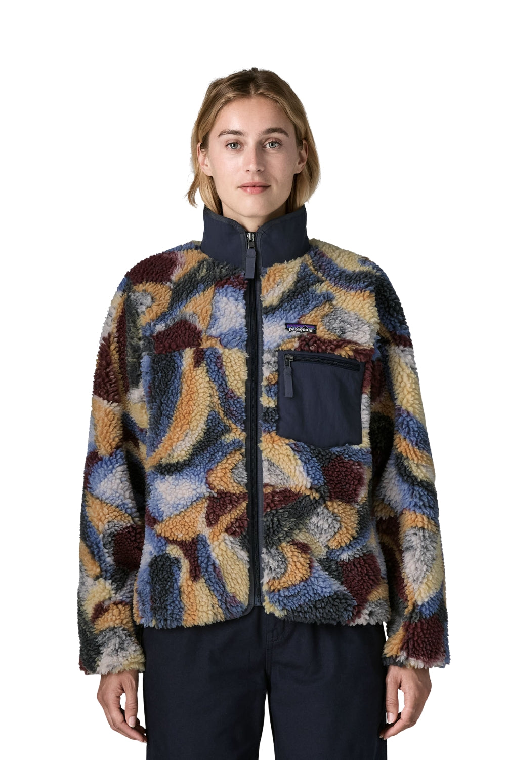 A model wearing a Patagonia fleece jacket with a multicolor abstract pattern in blue, yellow, brown, and gray, paired with dark navy pants, shot against a solid white background.