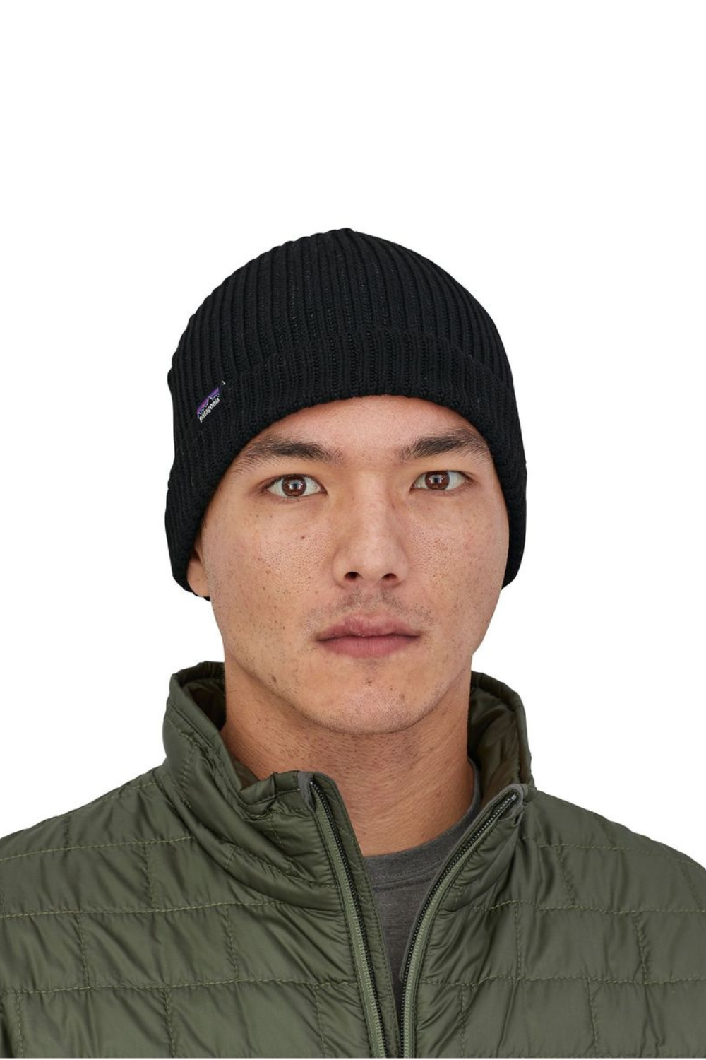 Person wearing a black knit beanie and green puffer jacket on a white background
