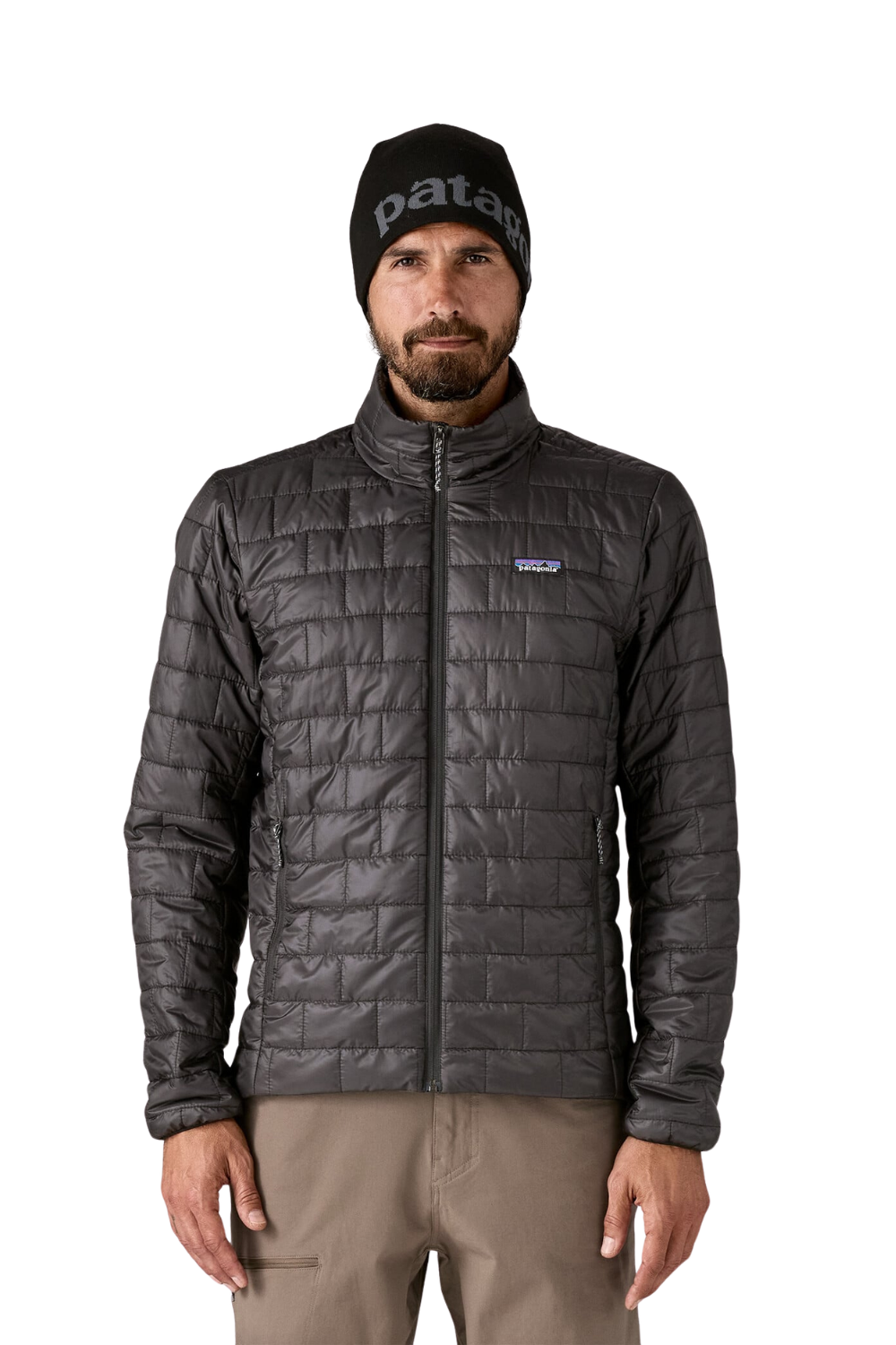 A man wearing a black Patagonia beanie and a dark gray Patagonia quilted jacket, paired with khaki pants, standing against a solid white background.