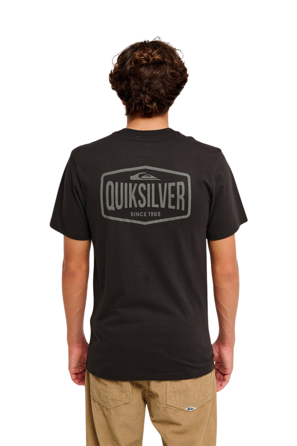 A man viewed from the back wearing a dark charcoal gray Quiksilver t-shirt with a large gray graphic logo on the back, paired with khaki pants, against a white background.