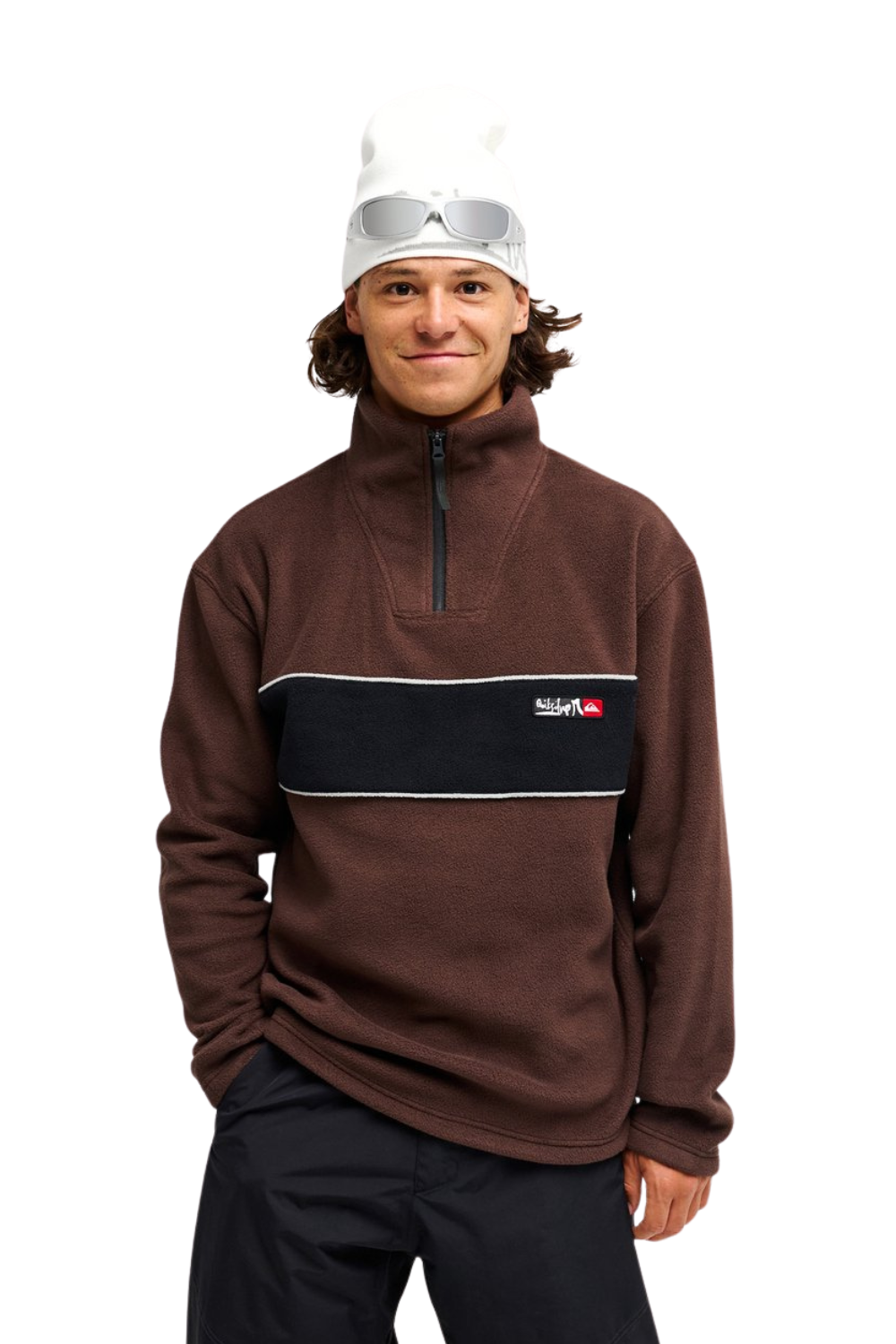 A man wearing a brown quarter-zip fleece pullover with a black chest stripe and a small red and white 'Quiksilver' logo, paired with a white beanie and sunglasses, against a plain white background.