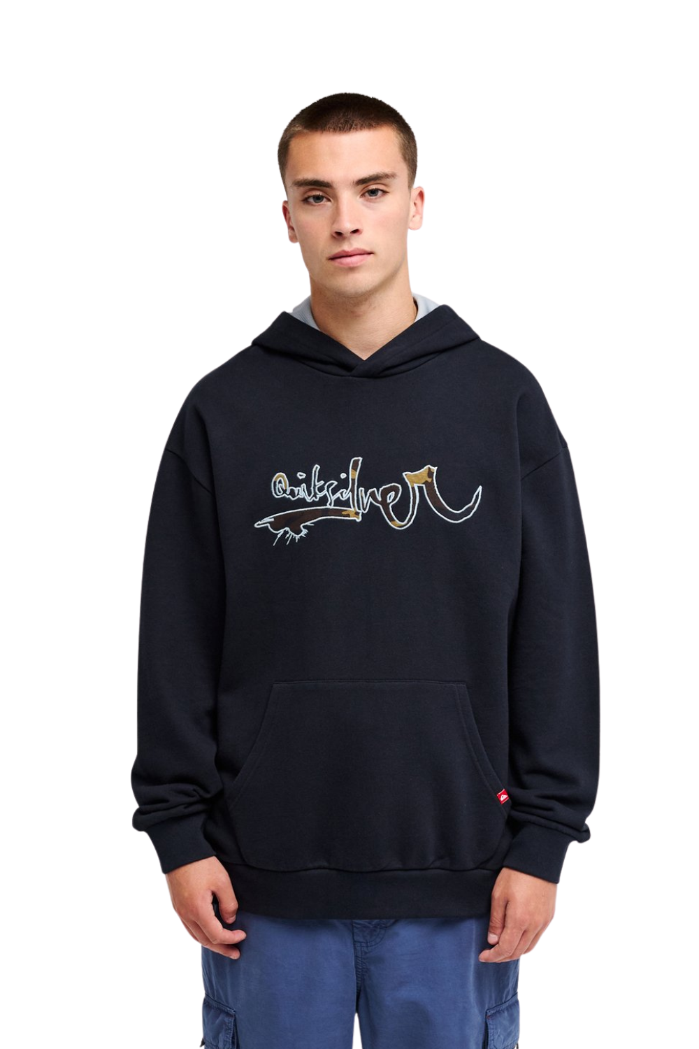 A man wearing a black pullover hoodie with a graphic Quiksilver logo on the chest, paired with blue jeans, photographed against a solid white background.