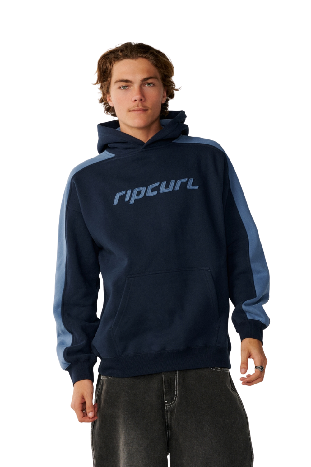 A man wearing a Rip Curl navy blue hoodie with light blue contrast panels on the shoulders and sleeves, and a light blue logo across the chest, paired with dark gray jeans against a white background.