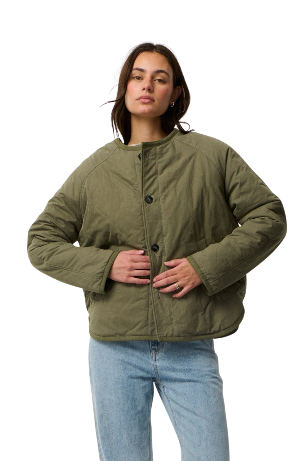 A woman modeling an olive green quilted jacket with black buttons, paired with light blue jeans, against a plain white background.