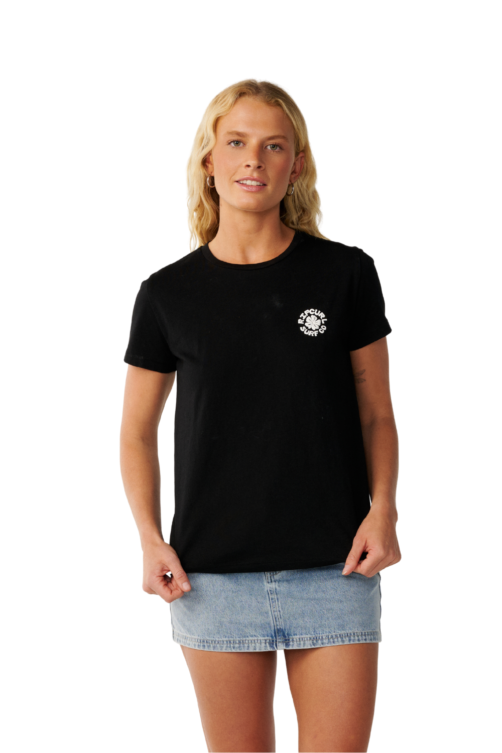 A woman modeling a black short-sleeve crewneck t-shirt with a small white circular graphic on the left chest, paired with a denim mini skirt, against a plain white background.