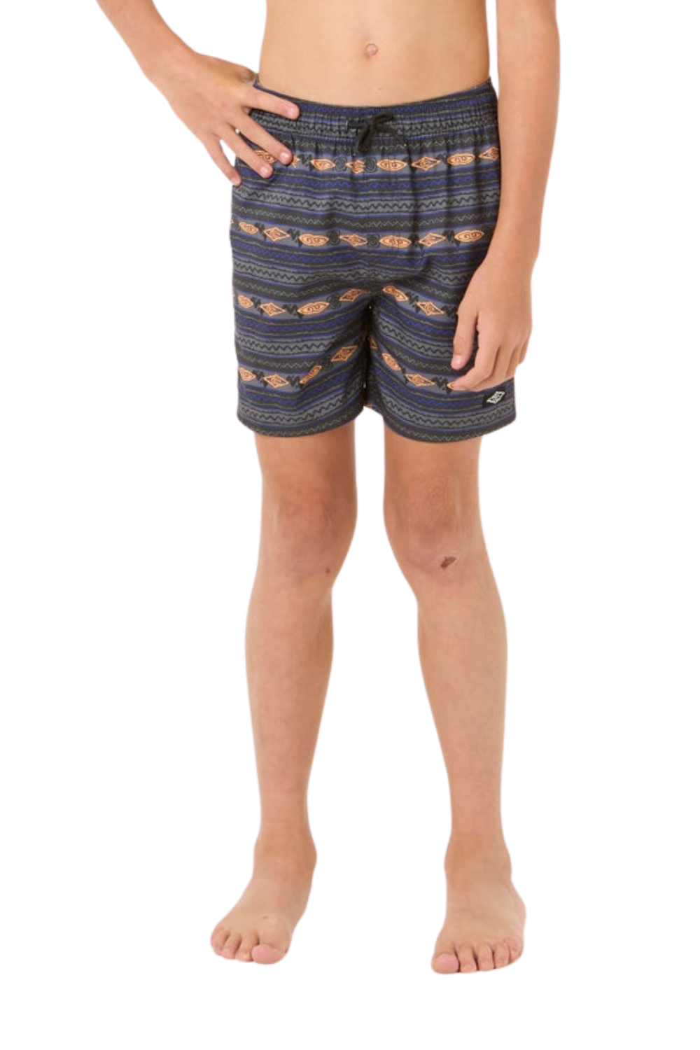 A child modeling patterned board shorts against a plain white background. The shorts feature a dark black/navy base with horizontal bands of orange, beige, and white geometric and floral motifs.