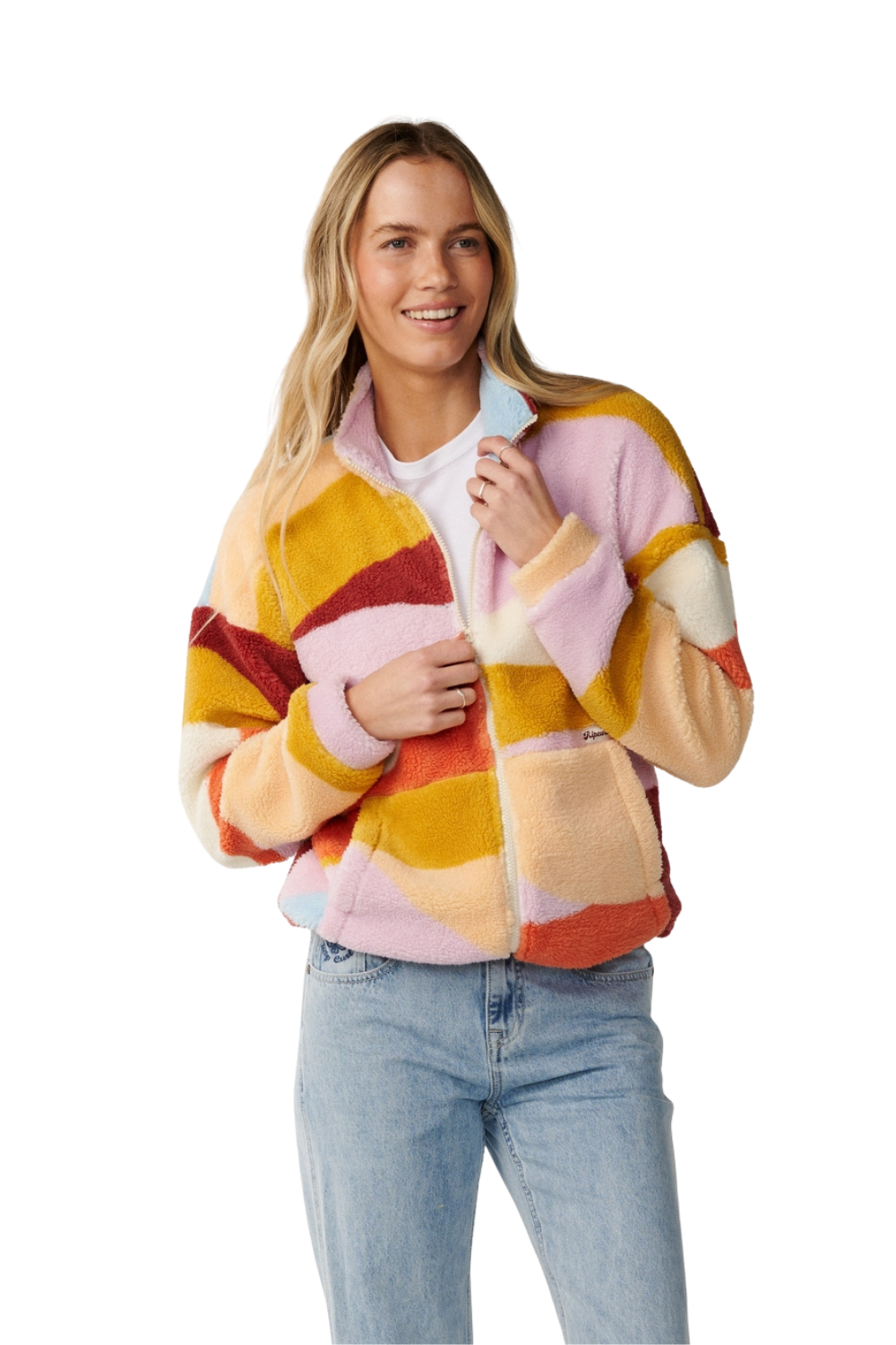 A woman wearing a fuzzy patch patterened zip-up fleece jacket in pastel  pink, yellow, orange, and cream, paired with light blue jeans, against a plain white background.